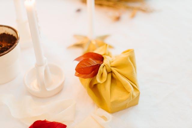 Cadeau emballé dans un furoshiki et customisé avec des feuilles séchée, posé sur une table de fête
