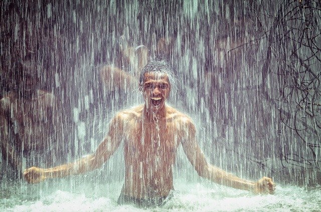Homme racisé torse nu sous une chute d'eau