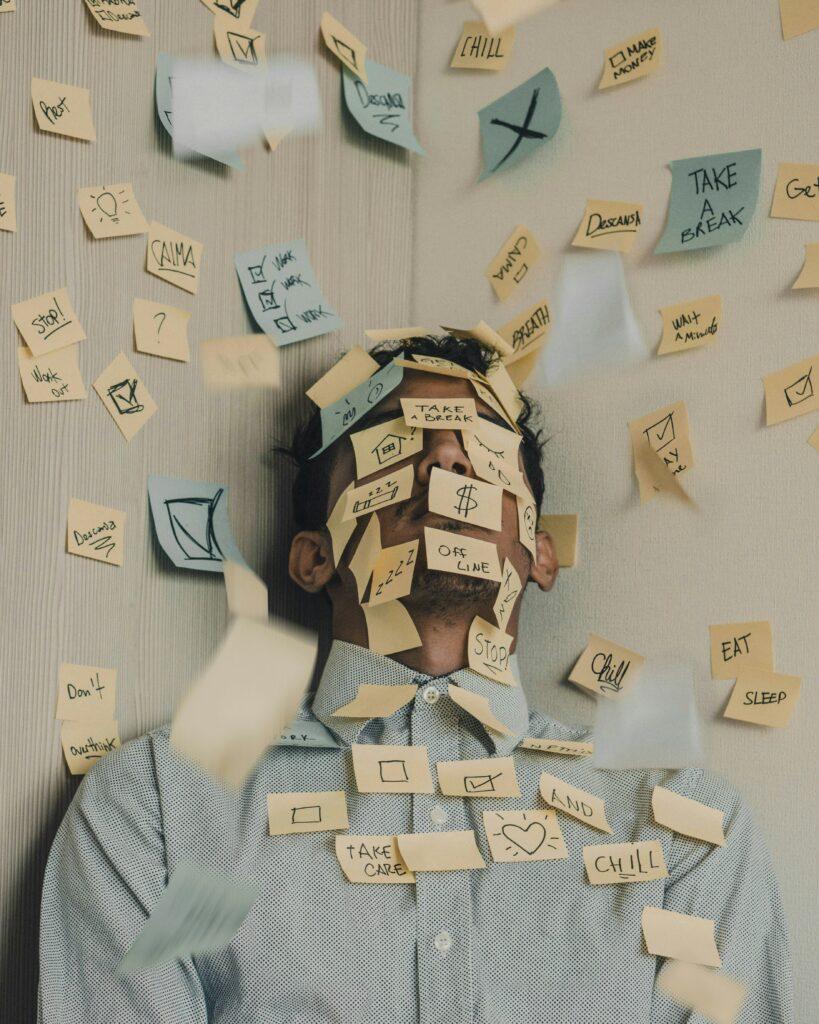 Photo d'un homme submergé de post-its, qui représente le surmenage et la charge mentale.